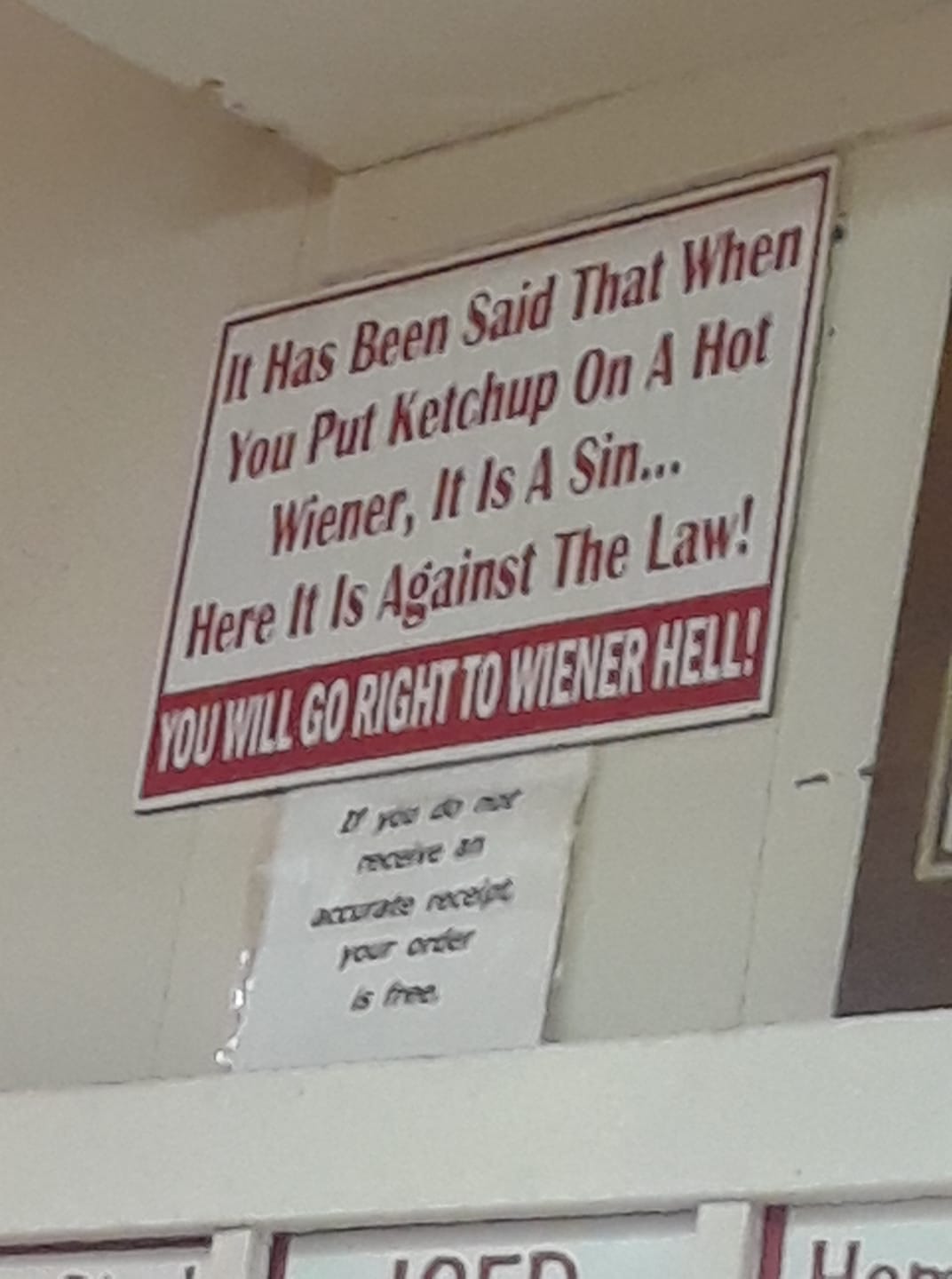 A sign in a hot dog stand in Rhode Island. The sign reads: "It Has Been Said That When You Put Ketchup On A Hot Wiener, It Is A Sin...Here It Is Against The Law! YOU WILL GO RIGHT TO WIENER HELL!"
